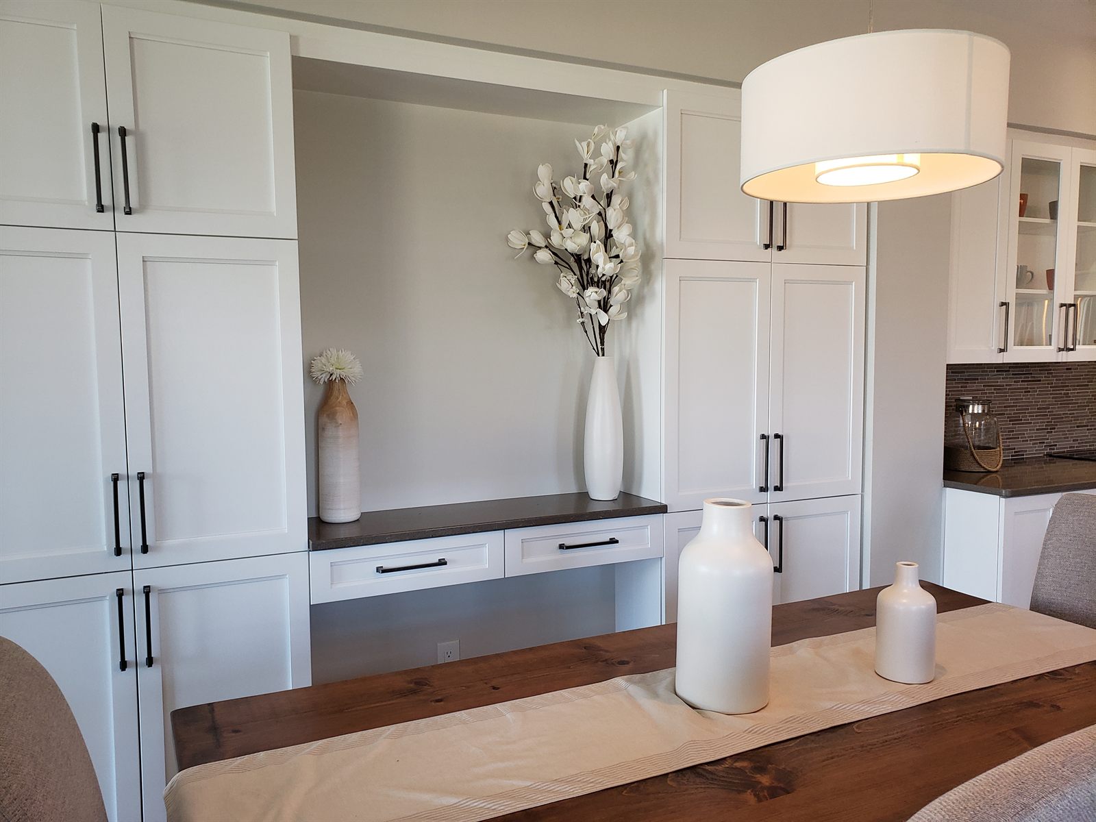 Witte inbouwkasten met een open nis, lades en een donker blad naast de eettafel