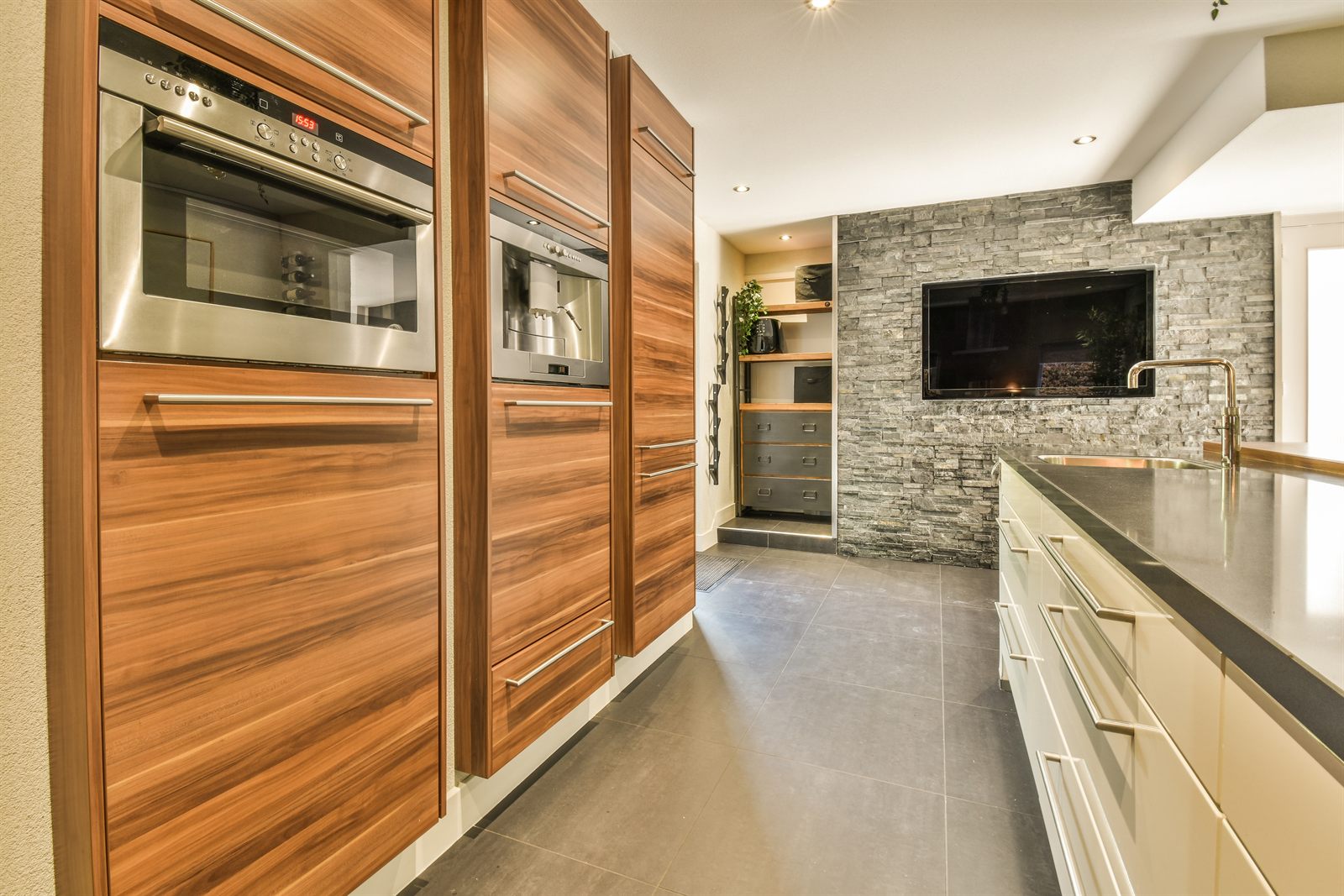Keuken met houten kastenwand, ingebouwde oven en koffiemachine, naast een stenen muur