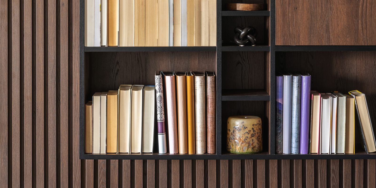 Wand met houten lamellen en open vakken met boeken